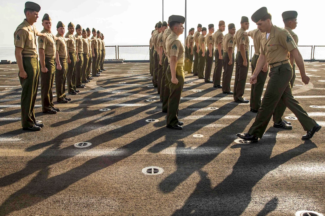 A platoon leader walks past his platoon as they stand at attention.