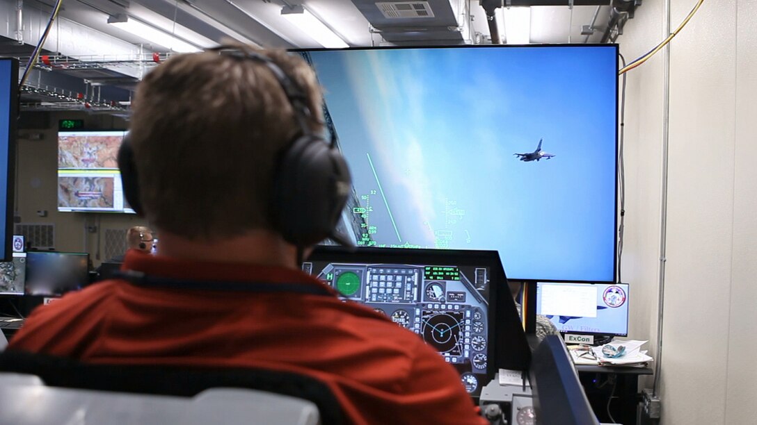 Donald Simones, a subject matter expert in the Air Force Research Laboratory’s 711th Human Performance Wing, flies a virtual F-16 in a Deployable Tactical Trainer during the Secure Live Virtual Constructive Advanced Training Environment (SLATE) Phase III capstone demonstration at Nellis Air Force Base, Nevada in September. The live aircraft, such as the one shown on the screen, were able to see and interact with the virtual players like Simones during the demonstration. (U.S. Air Force photo/William Graver)