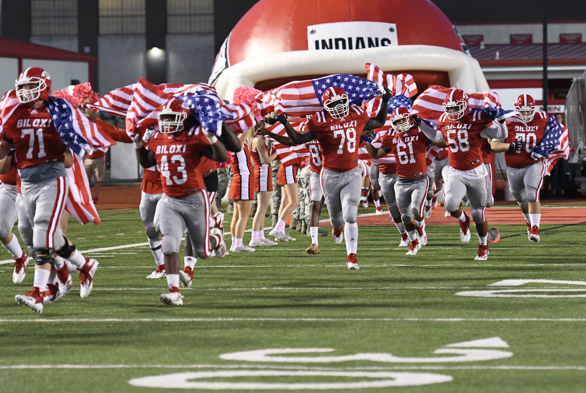 Members of the Biloxi High School Football Team run onto the field carrying U.S Flags during the Biloxi High School military appreciation night football game in Biloxi, Mississippi, Oct. 5, 2018. Keesler personnel also participated in holding the U.S. Flag during the playing of the national anthem and the coin toss to determine which team would receive the ball first. (U.S. Air Force photo by Kemberly Groue)