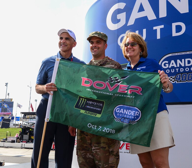 Tech. Sgt. Michael Kelly, 736th Aircraft Maintenance Squadron, C-17 Globemaster III flight line expediter, receives the green flag from Mike Tatoian, Dover International Speedway president and CEO, and Tamara Ward, Camping World Holdings Inc. executive vice president of corporate development, at the “Gander Outdoors 400” Monster Energy NASCAR Cup Series race Oct. 7, 2018, at the Dover International Speedway in Dover, Del. Kelly was named the honorary starter for the race by DIS officials to honor his military service and to represent Dover Air Force Base at the event. (U.S. Air Force photo by Airman First Class Dedan D. Dials)