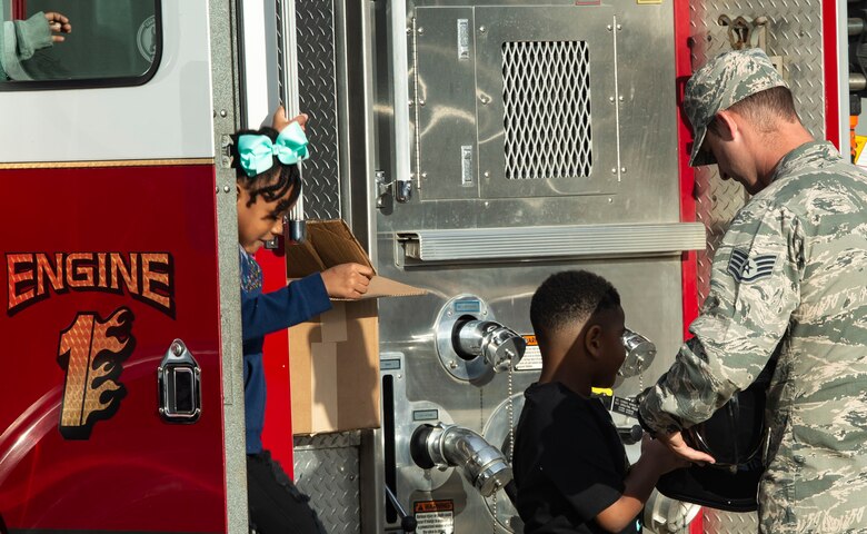U.S. Air Force Staff Sgt. Christopher Crusius, 20th Civil Engineer Squadron fire department crew chief, hands Shaw Heights Elementary School students junior firefighter helmets during a Fire Prevention Week visit at Shaw Air Force Base, S.C., Oct. 9, 2018.