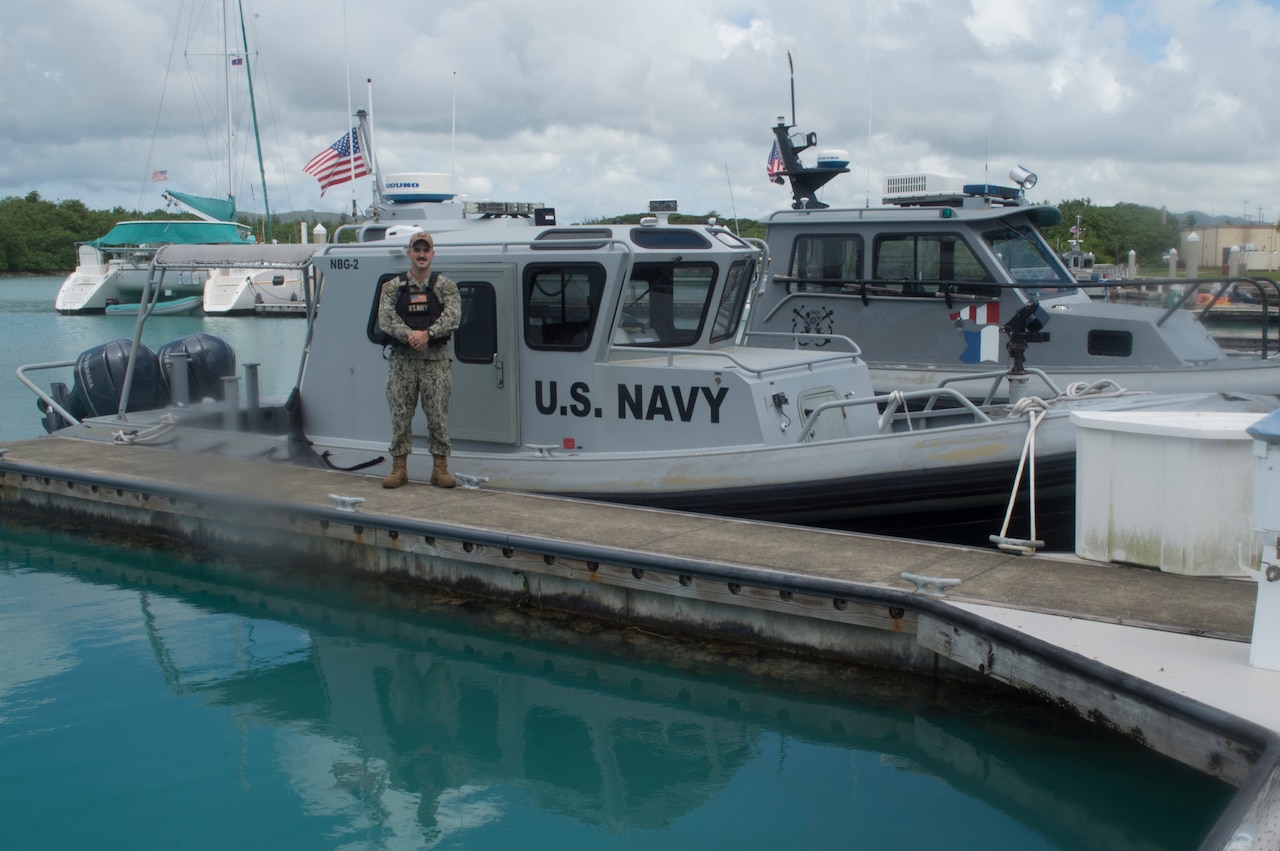 A Navy petty officer poses in front of a boat.