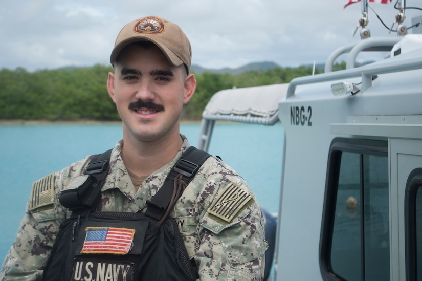 A Navy petty officer poses in front of a boat.