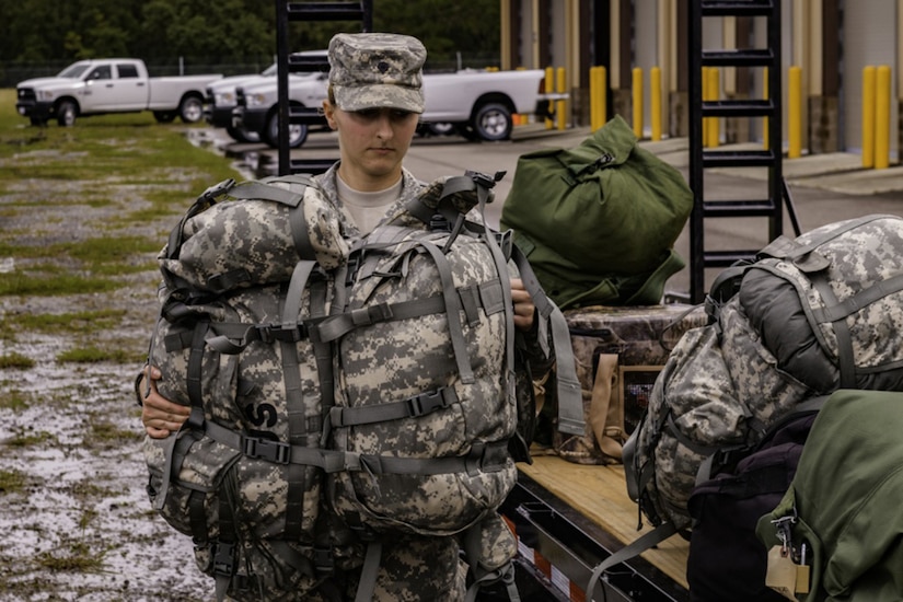 A female soldier places backpacks on a truck.