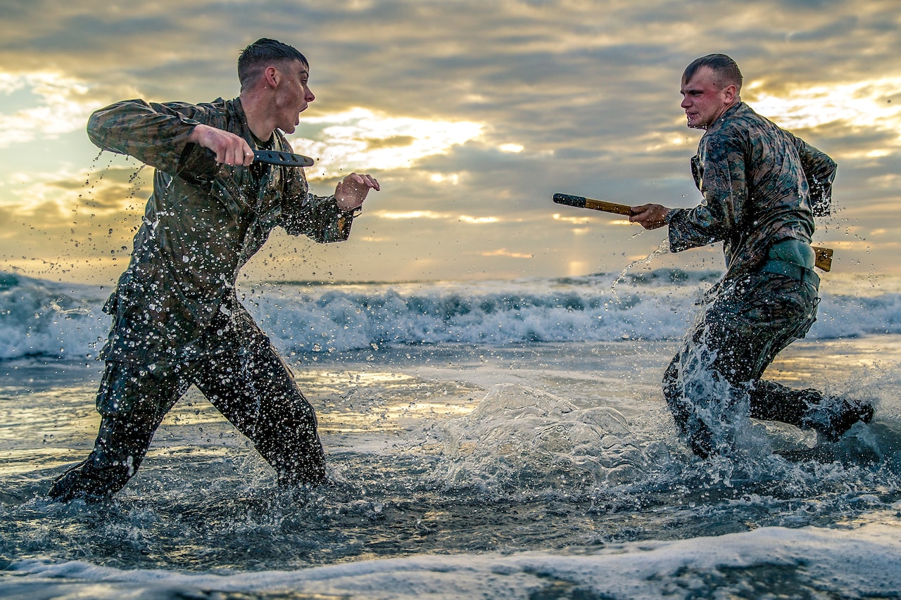 Two Marines spar along the edge of the water on a beach.