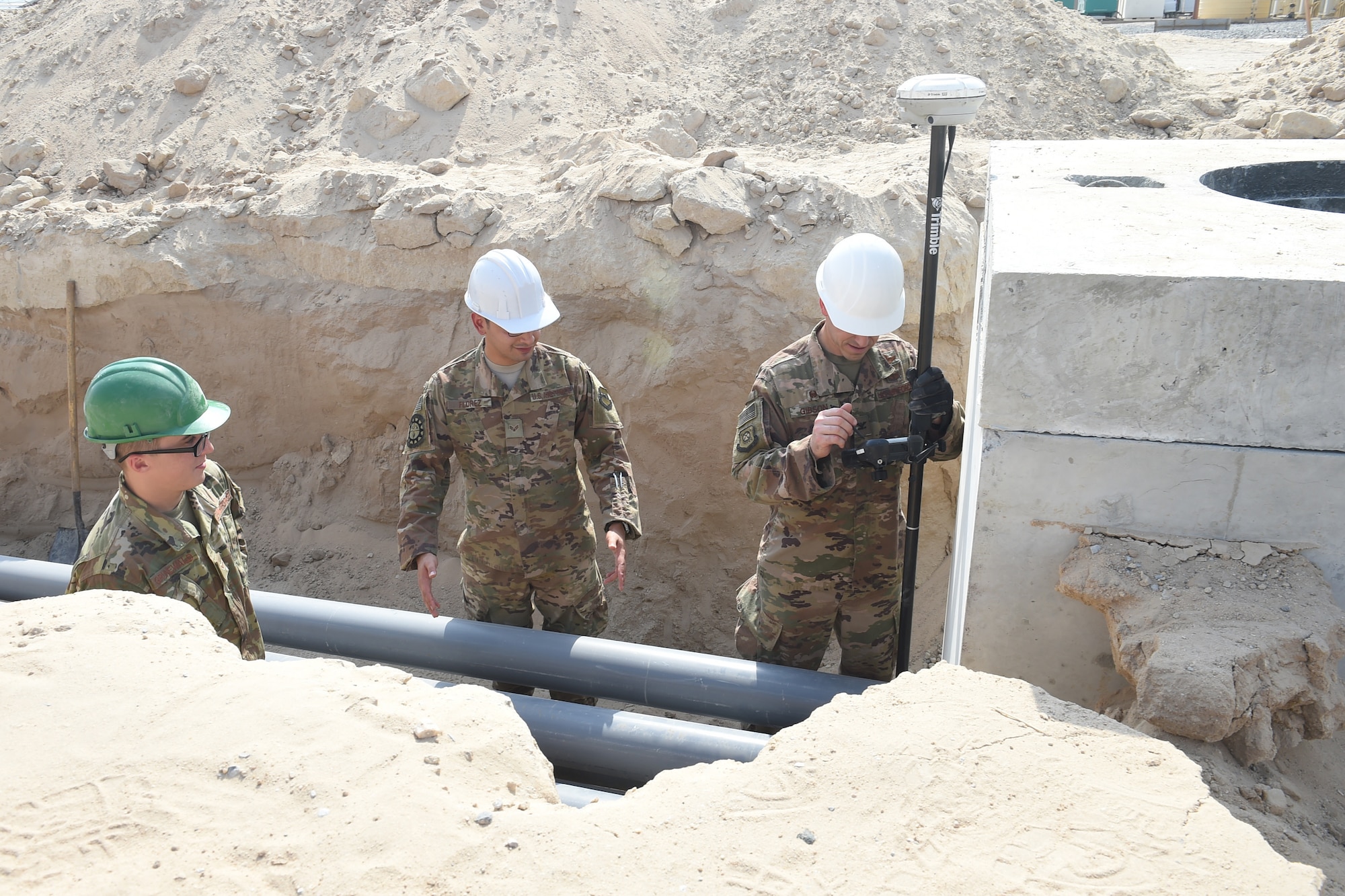Three Airmen use an engineering tool outside.