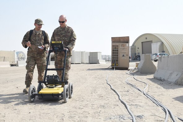 Three Airmen use an engineering tool outside.