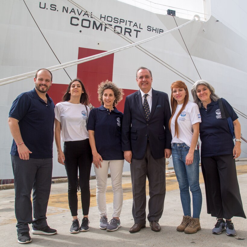 Ambassador Alejandro Daneri, president, White Helmets Commission of Argentina, poses for a group photo with members of the White Helmets Commission of Argentina in front of USNS Comfort (T-AH 20).