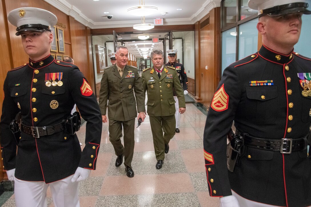 Marine Corps Gen. Joe Dunford walks with a foreign service member in a hallway behind two Marines.