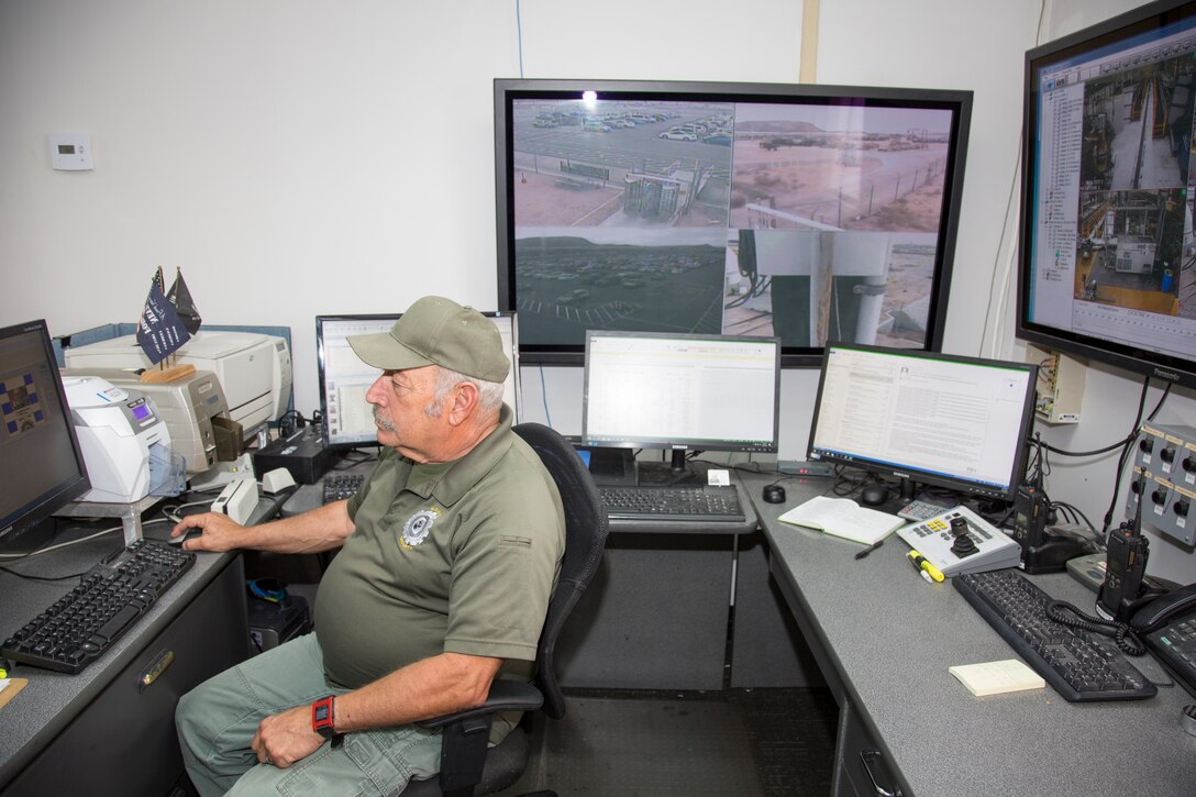 Michael Hass, access control officer, Security Department, prepares to issue an access card as remote cameras scan the grounds and interior at Production Plant Barstow, Oct. 3. The Marine Depot Maintenance Command Facility aboard the Yermo Annex of Marine Corps Logistics Base Barstow, Calif., has a full-time security staff keeping an eye on the property and people working at the Plant.
