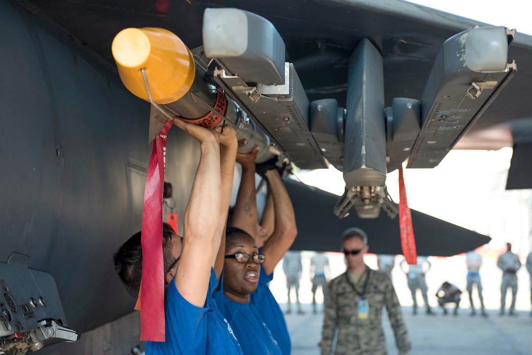 Airmen hoist a missile over their heads while attaching it to an aircraft wing.