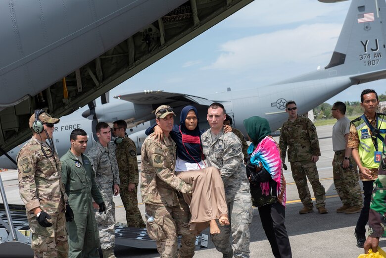 U.S. Air Force Staff Sgt. Jeffery Miller and Airman 1st Class Anthony Benitez, both assigned to Yokota Air Base, Japan carries an injured Indonesian woman from a C-130 Hercules aircraft in Balikpapan, Indonesia Oct. 9, 2018.