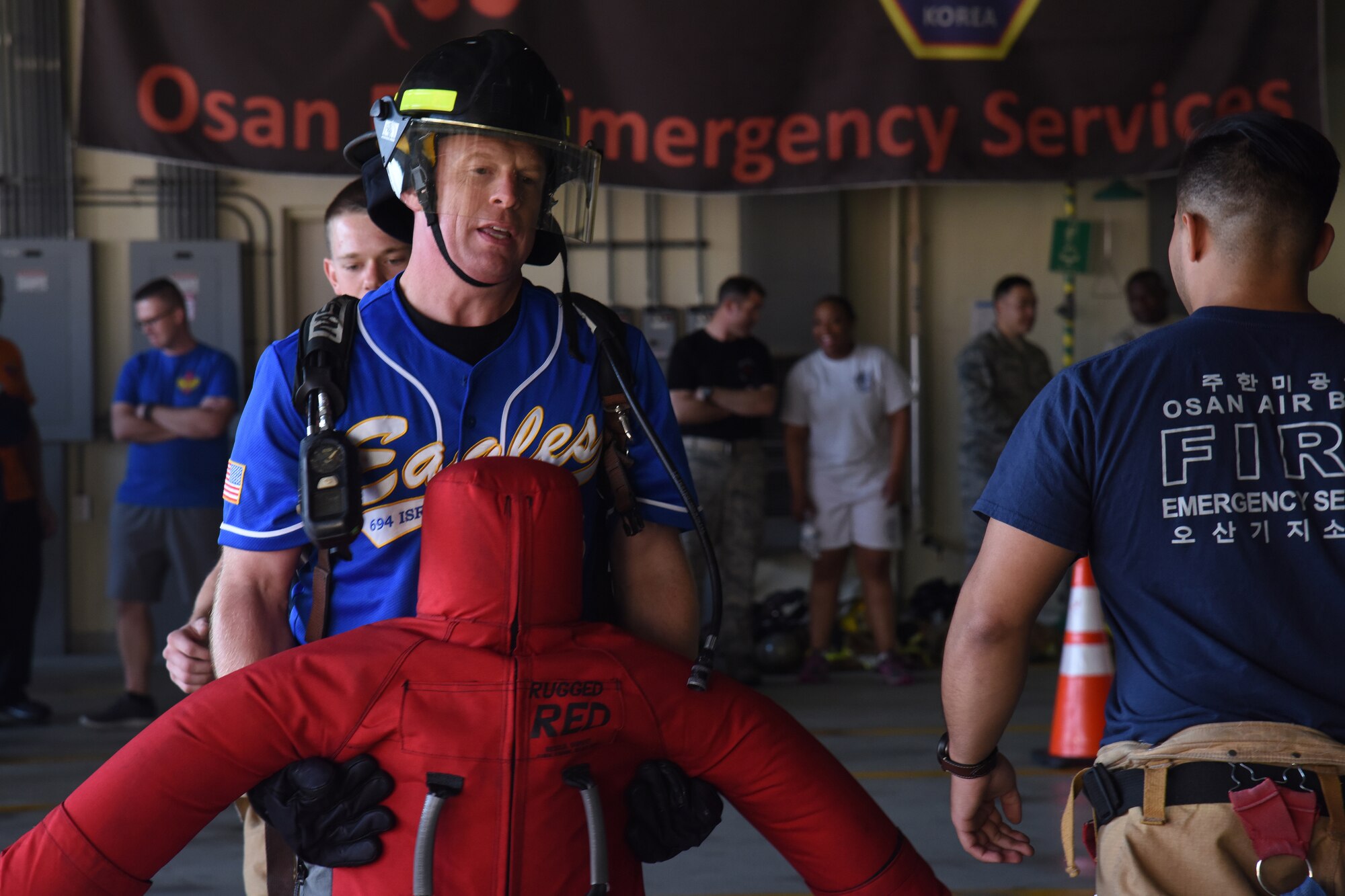 U.S. Air Force Col. Lester Oberg, commander of the 694th Intelligence, Surveillance and Reconnaissance Group carries a training dummy to the finish line as Airman Joseph Jenkins, behind, and Staff Sgt. Jonathan Martinez, far right, 51st Civil Engineer Squadron fire and emergency services flight firefighters, watch for safety precautions during the Eagles and Commanders versus Chiefs and Shirts Fire Muster at Osan Air Base, Republic of Korea, Oct. 12, 2018. The event was one of many planned by the 51st Civil Engineer Squadron fire and emergency services team for Fire Prevention Week, which was held 9 through 13 Oct. (U.S. Air Force photo by Tech. Sgt. Ashley Tyler)
