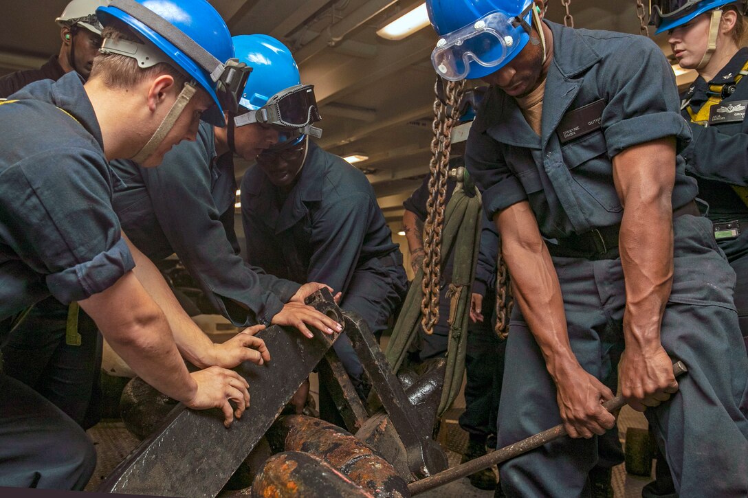 Five sailors work together to attach a stopper to an anchor chain.