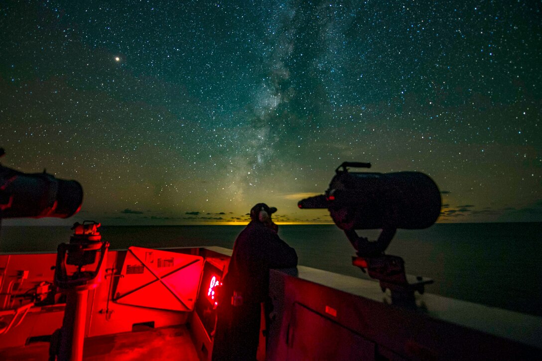 A sailor peers out over the open sea at night.