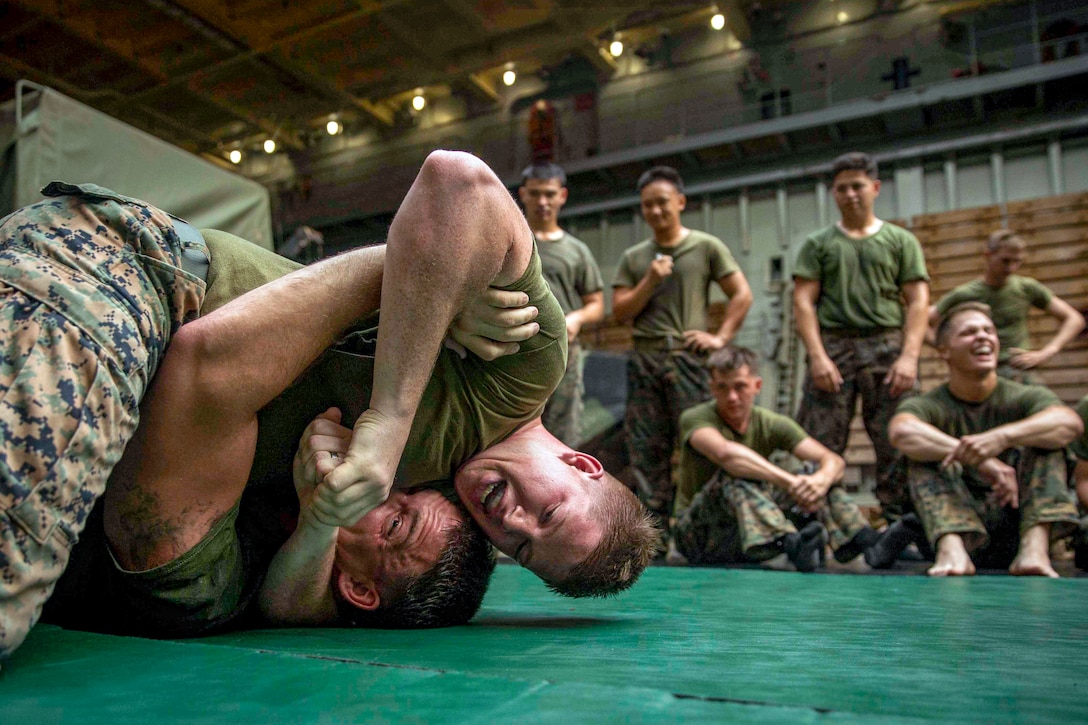 Several Marines watch two other Marines grapple on the ground.