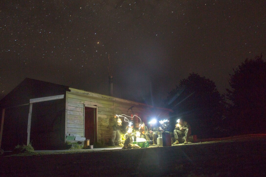 Marines gather for an evening meal in front of a wooden building at night.