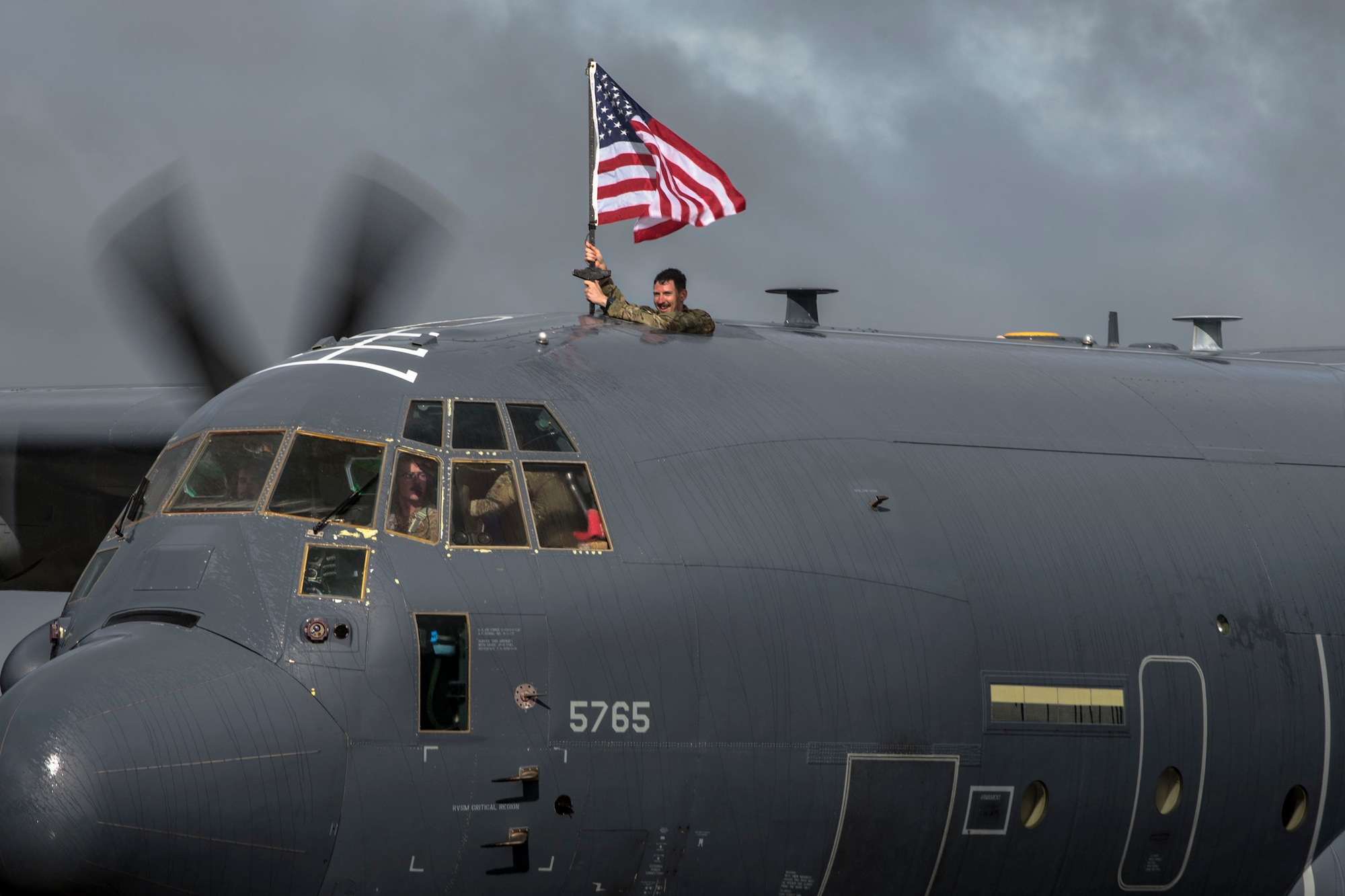 Capt. David Schmitt, 71st Rescue Squadron (RQS) HC-130J combat systems officer, waves a flag out of an HC-130J Combat King II during a redeployment ceremony, Oct. 9, 2018, at Moody Air Force Base, Ga. The 71st RQS maintains combat-ready status and provides deployable personnel recovery forces to theater commanders for contingency and crisis response operations worldwide. (U.S. Air Force photo by Airman Taryn Butler)