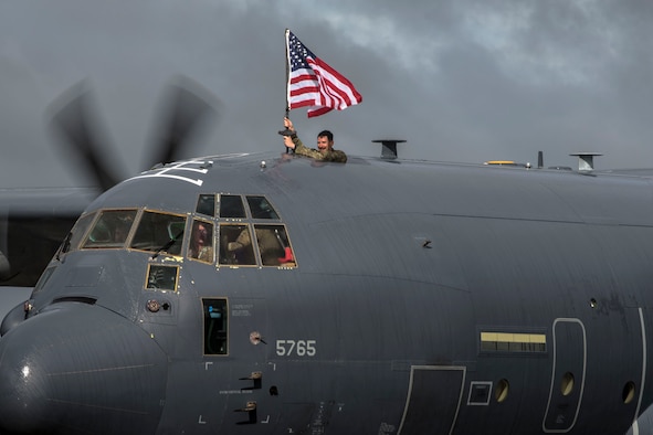 Capt. David Schmitt, 71st Rescue Squadron (RQS) HC-130J combat systems officer, waves a flag out of an HC-130J Combat King II during a redeployment ceremony, Oct. 9, 2018, at Moody Air Force Base, Ga. The 71st RQS maintains combat-ready status and provides deployable personnel recovery forces to theater commanders for contingency and crisis response operations worldwide. (U.S. Air Force photo by Airman Taryn Butler)