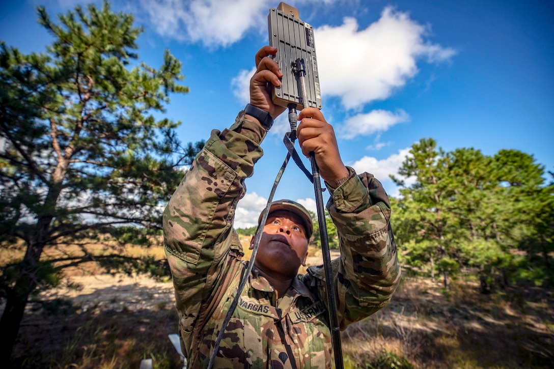 A solder places an antenna on a stand in a field.