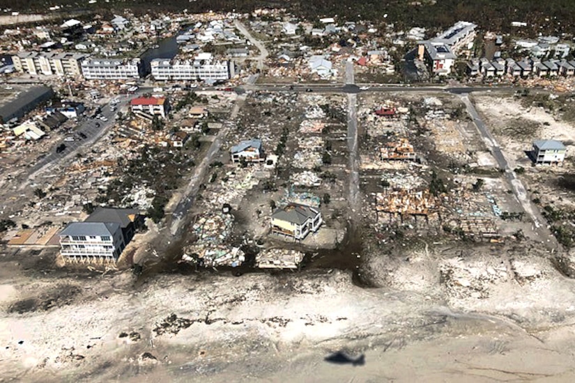 Damaged and destroyed homes dot the coastline of a beach, visible from overhead.