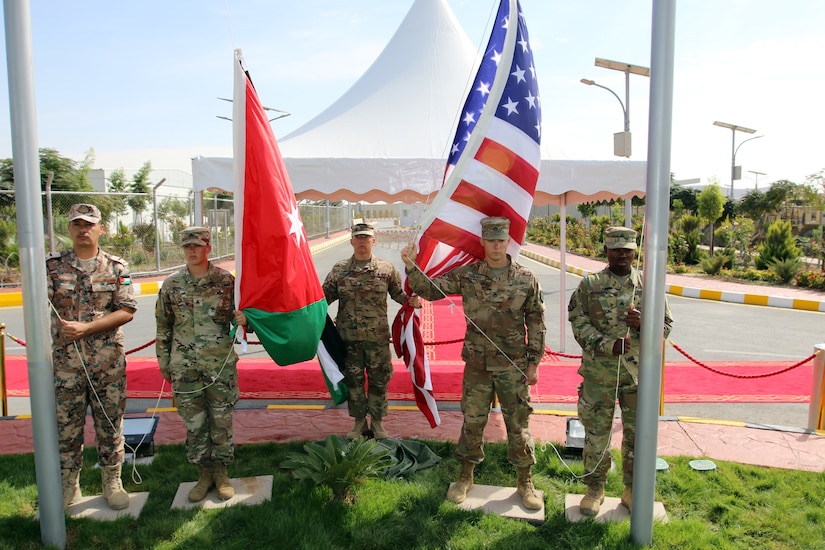 A flag-raising detail stands ready during a dedication ceremony for an expansion of the Jordan Armed Forces Joint Training Center on Oct. 10, 2018. The detail was comprised of, from left: Chief Ibrahim Shuquirat, with the noncommissioned officer academy, Jordan Armed Forces; and U.S. Army personnel Sgt. Jennifer Kutcher, Headquarters Support Company, Headquarters and Headquarters Battalion, 28th Infantry Division, Pa. Army National Guard; Staff Sgt. Henry Moeller, Bravo Company, HHBN, 28 ID (the detail’s noncommissioned officer in charge); Staff Sgt. Joseph Santas, 728th Engineer Detachment, 416th Theater Engineer Command, U.S. Army Reserve; and Sgt. Braima Massaquoi, 151st Regional Support Group, Massachusetts Army National Guard.