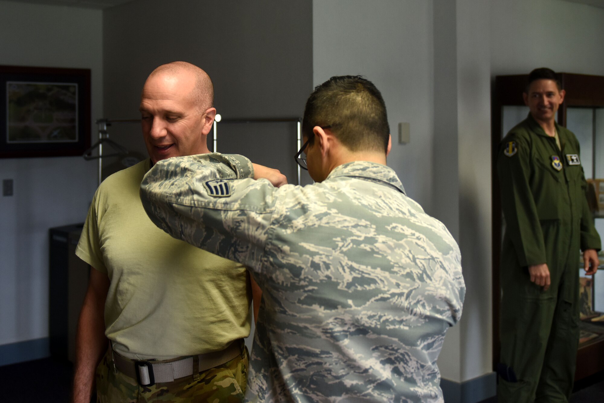 A man wearing a sand t-shirt receives a shot from a man with dark hair and glasses wearing the Airman Battle Uniform.