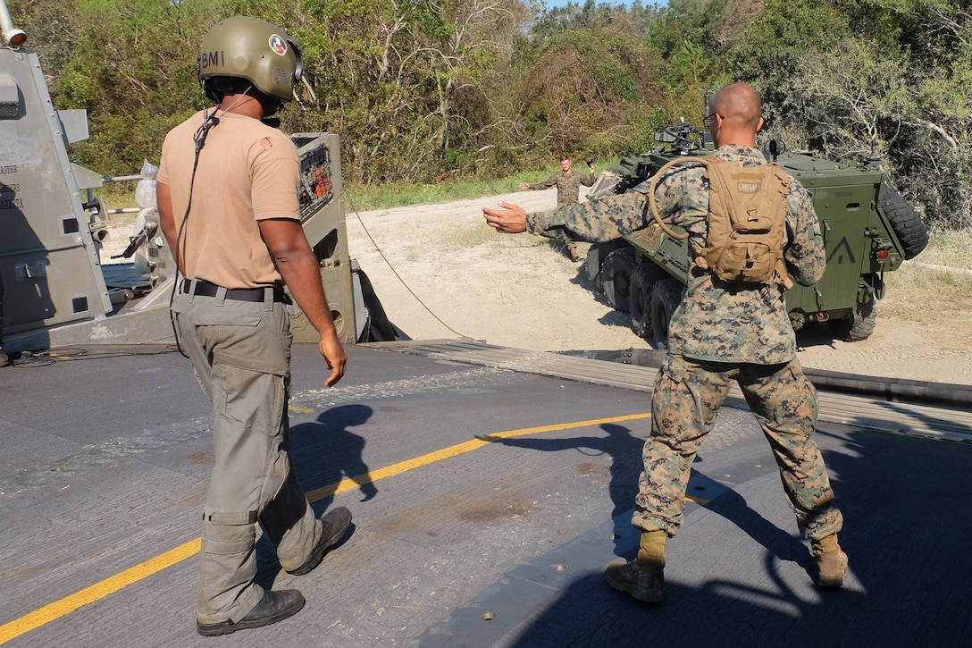 A U.S. Marine and Sailor guide a Light Armored Vehicle onto the loading ramp of a Landing Craft Air Cushion at Mile Hammock Bay, Camp Lejeune, North Carolina, Oct. 5, 2018 during Type Commander Amphibious Training. TCAT allows the 24th Marine Expeditionary Unit, their subordinate units, and the U.S. Navy’s Iwo Jima Amphibious Ready Group to rehearse ship to shore maneuver and expeditionary command and control prior to exercise Trident Juncture 2018. The goal of TCAT is to increase unit and individual proficiency during amphibious operations. The LAVs are with 2nd Light Armored Reconnaissance Battalion, 24th Marine Expeditionary Unit.  (U.S. Marine Corps photo by Gunnery Sgt. Robert Durham/released)