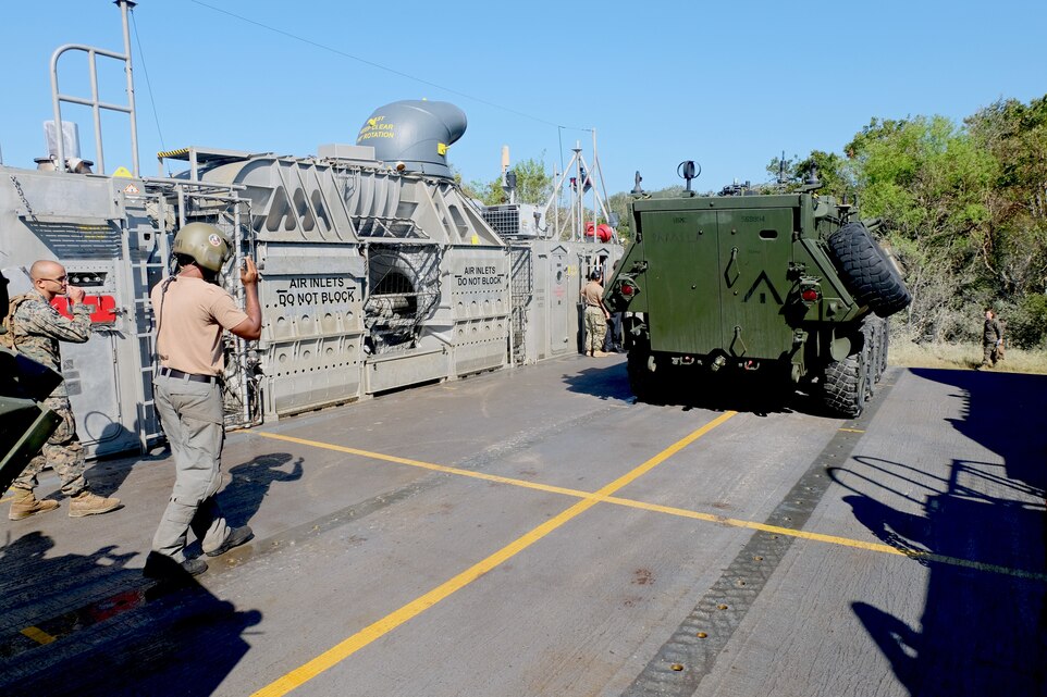 A U.S. Marine and Sailor guide a Light Armored Vehicle onto the loading ramp of a Landing Craft Air Cushion at Mile Hammock Bay, Camp Lejeune, North Carolina, Oct. 5, 2018 during Type Commander Amphibious Training. TCAT allows the 24th Marine Expeditionary Unit, their subordinate units, and the U.S. Navy’s Iwo Jima Amphibious Ready Group to rehearse ship to shore maneuver and expeditionary command and control prior to exercise Trident Juncture 2018. The goal of TCAT is to increase unit and individual proficiency during amphibious operations. The LAVs are with 2nd Light Armored Reconnaissance Battalion, 24th Marine Expeditionary Unit.  (U.S. Marine Corps photo by Gunnery Sgt. Robert Durham/released)