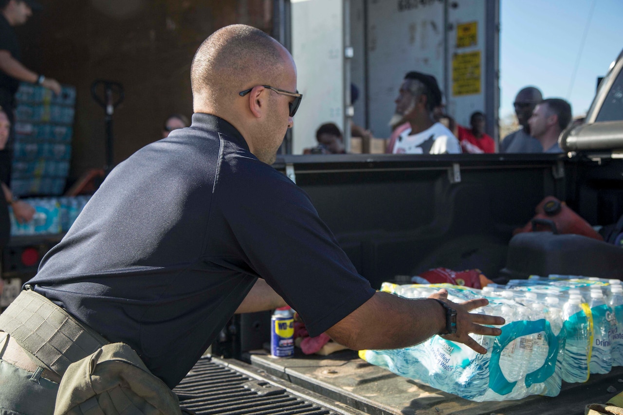 A man puts a case of bottled water into the back of a pickup truck.