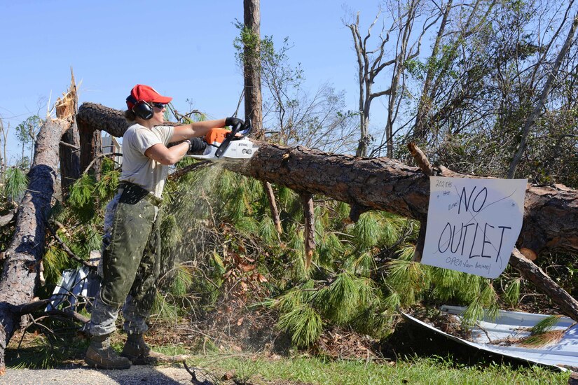 An Air Force engineer saws through a felled tree using a chainsaw.