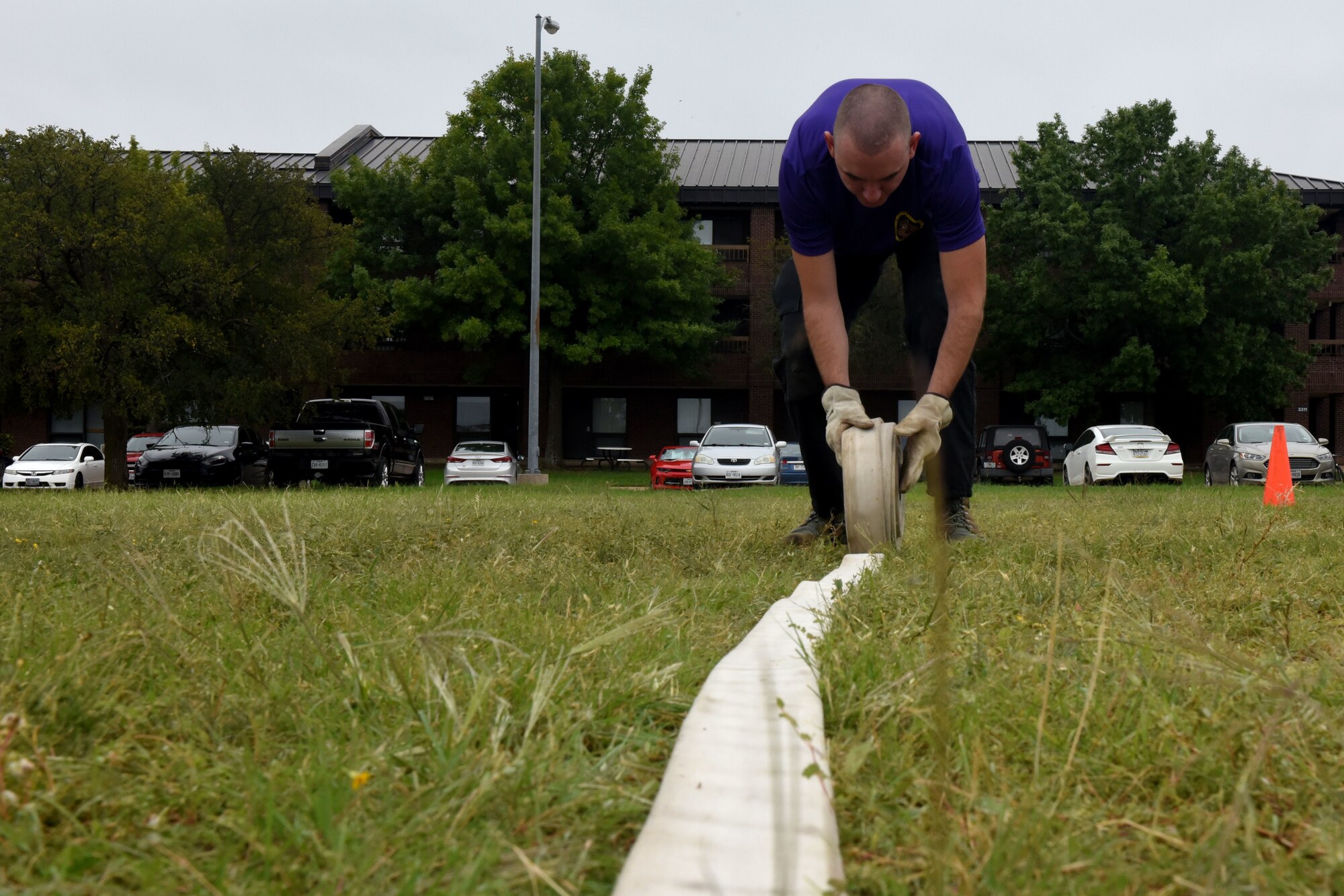 U.S. Air Force Senior Airman Randall Moose, 17th Training Wing Public Affairs photojournalist, rolls up a 100-foot long fire hose during the 13th Annual Fire Muster on Goodfellow Air Force Base, Texas, Oct. 12, 2018. After completing the roll, Moose had to step on the fire hose so his team could move on to the next obstacle. (U.S. Air Force photo by 2nd Lt. Matthew Stott/Released)