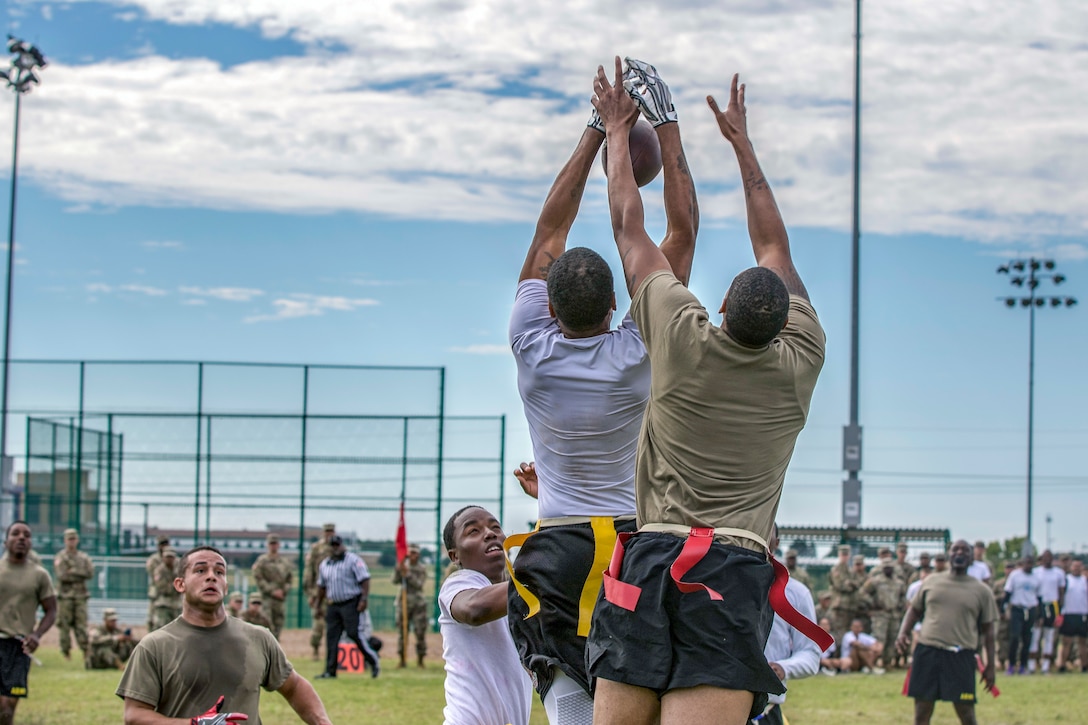 Two soldiers jump to catch a football pass.