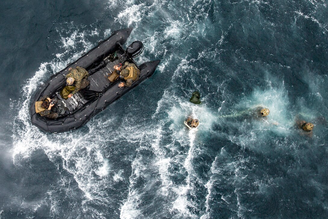 Seen from above, marines swim toward a rubber boat in the open ocean.