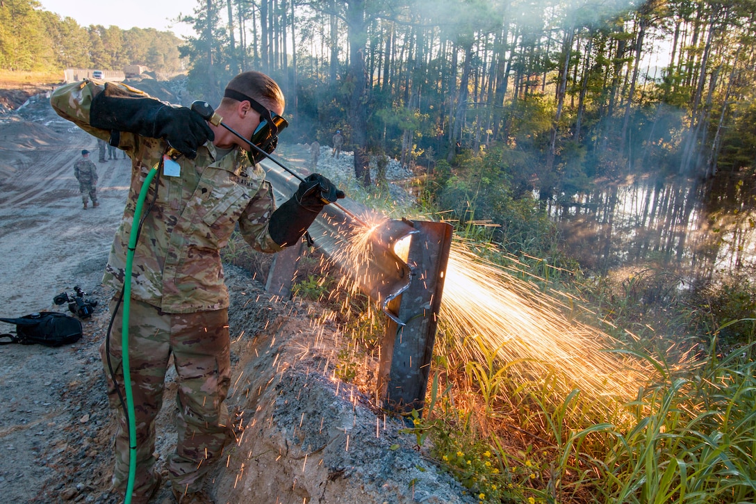 A soldier cuts through  guardrail and sprays sparks evenywhere.