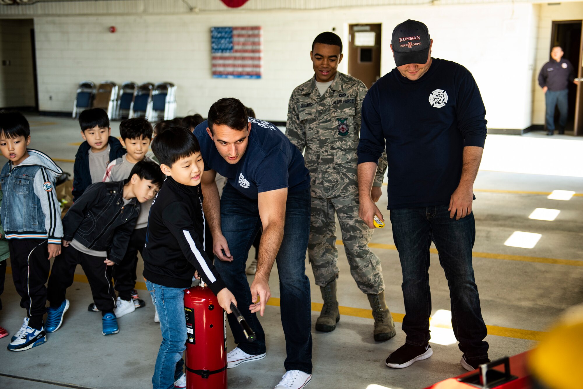 U.S. Air Force Staff Sgt. Phillip Barmann, 8th Civil Engineering Squadron fire crew chief, helps a student from Su Song Elementary put out a simulated fire at an open house on Kunsan Air Base, Republic of Korea, Oct. 11, 2018. Fire extinguishers are typically the first resort in trying to put out fires in an emergency. (U.S. Air Force photo by Senior Airman Stefan Alvarez)