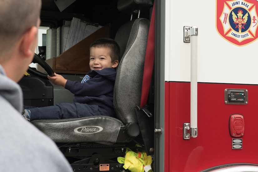 Aliyas Hall, age 2, smiles at his dad, U.S. Army Pvt. Nicholas Hall, 331st Transportation Company, 11th Transportation Battalion, 7th Transportation Brigade (Expeditionary) watercraft operator, from the seat of a fire truck during the Fort Eustis Fire and Emergency Services Open House event at Joint Base Langley-Eustis, Va., Oct. 13, 2018.