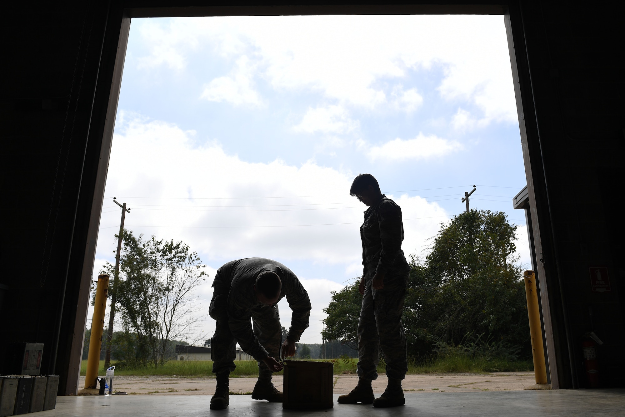 A man bends down to open a box, while a female stands and watches.