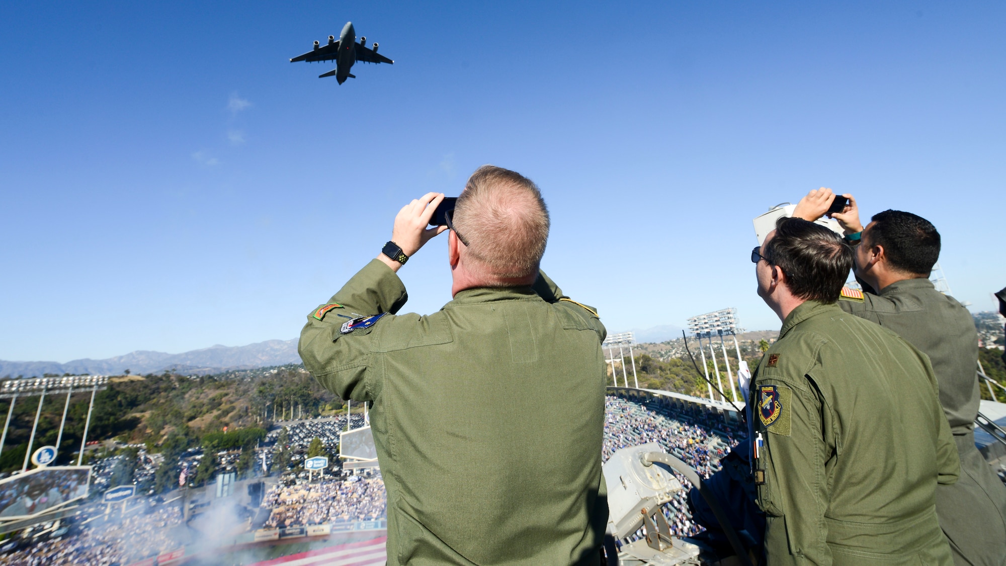 A C-17 Globemaster flies over Dodger Stadium during the opening ceremony of Game 3 of Major League Baseball’s National League Championship Series between the Los Angeles Dodgers and Milwaukee Brewers at Dodger Stadium in Los Angeles, California, Oct. 15. The C-17 began its flight from Edwards Air Force Base. Master Sgt. Caleb Patterson, Maj. Duncan Reed and Tech Sgt. Robert Villa (left to right), all with 418th Flight Test Squadron, 412th Test Wing, coordinated with the C-17’s flight crew to time the plane’s flyover with singing of the National Anthem. (U.S. Air Force photo by Giancarlo Casem)