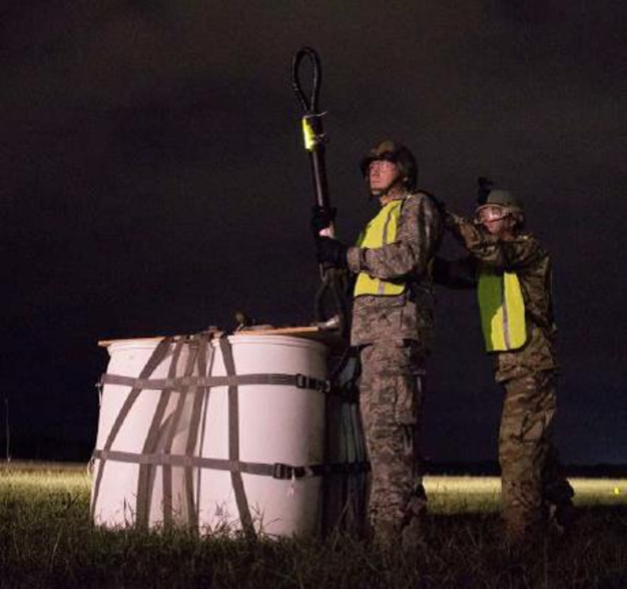 Capt. Nathan Del Rio (right) braces 2nd Lt. Brandon Smolinski as they attach a 2,000 pound A-22 cargo bag of supplies to a UH-60 Black Hawk helicopter