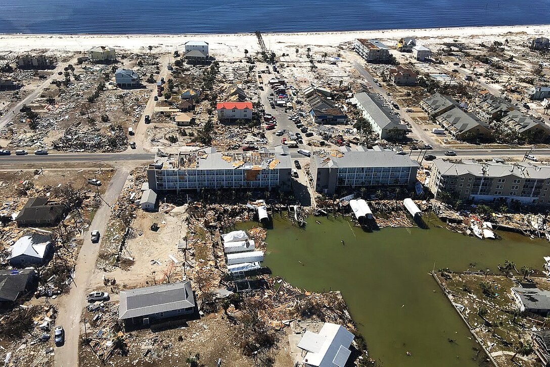An aerial view shows devastated buildings along a sandy coast.