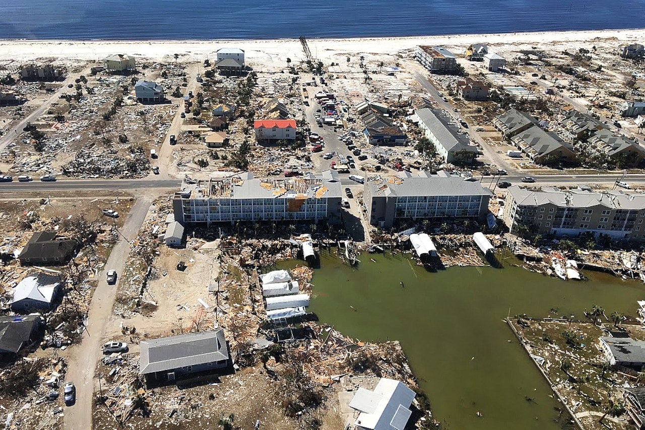An aerial view shows devastated buildings along a sandy coast.