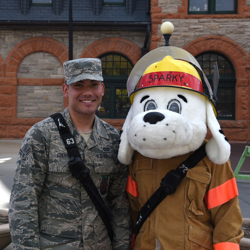 Airman 1st Class Anthony Ebersole stands with Sparky at the Fire Prevention Week Open House on Oct. 13, 2018 at the Depot Plaza, Cheyenne, Wyo. These two individuals represented F. E. Warren Air Force Base and passed on vital safety information to the patrons attending the event. TIP: Test alarms at least once a month by pressing the test button.