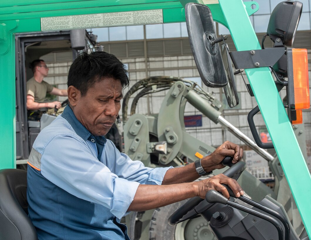 An Indonesian man drives a forklift as U.S. Staff Sgt Raymond Haynes, 36th Mobility Response Squadron aerial porter, at Andersen Air Force Base, Guam simultaneously drives another in the background in Balikpapan, Indonesia Oct. 12, 2018. The picture represents the joint and multinational effort needed to support the disaster relief missions in Indonesia. Members from the 36th Contingency Response Group worked and trained alongside host nation partners to ensure supplies were delivered immediately to thousands of Indonesians affected by a recent tsunami and earthquake. (U.S. Air Force photo by Master Sgt. JT May III)