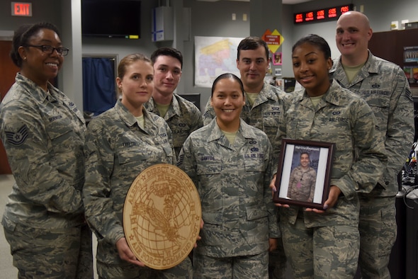 Seven Airmen wearing the Airmen Battle Uniform hold up a command post sign made of wood and a photo of an Airman down range.