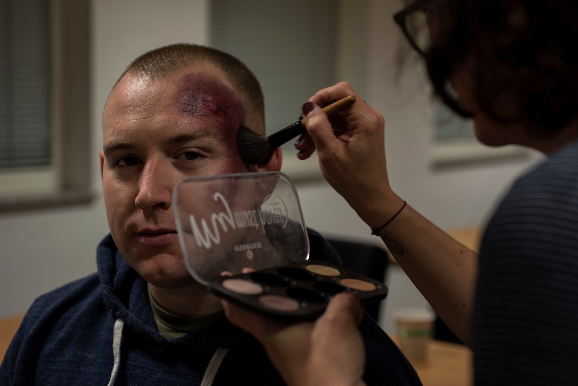 Connie Kurtze, 52nd Medical Operations Squadron family advocacy program assistant, right, applies moulage makeup to U.S. Air Force Tech. Sgt. Jeremy Lundgren, 52nd Force Support Squadron academic affairs NCO in-charge, left, at Spangdahlem Air Base, Germany, Oct. 17, 2018. Lundgren wore the simulated injury for one day in support of the Black Eye Campaign, a social experiment to see how many people notice signs of domestic violence. Each volunteer recorded how many people approached them and in what way. (U.S. Air Force photo by Airman 1st Class Valerie Seelye)