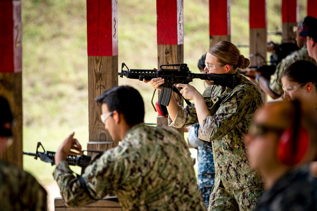Service members aim rifles on an outdoor filing line.