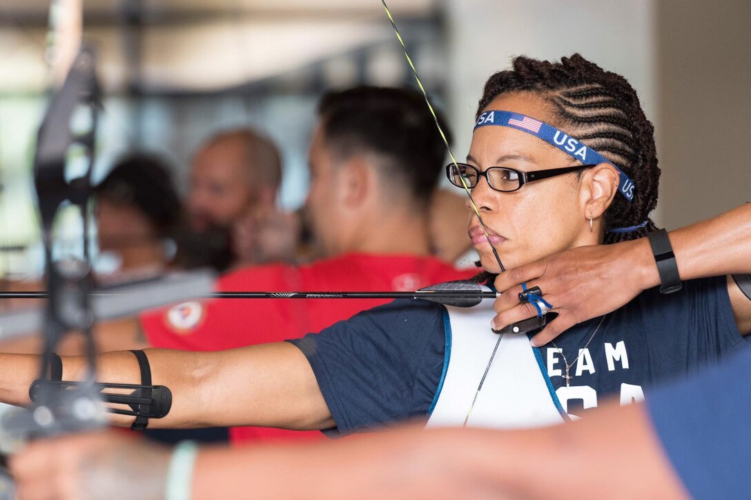 An archer pulls an arrow back in her bow and aims with one eye closed.