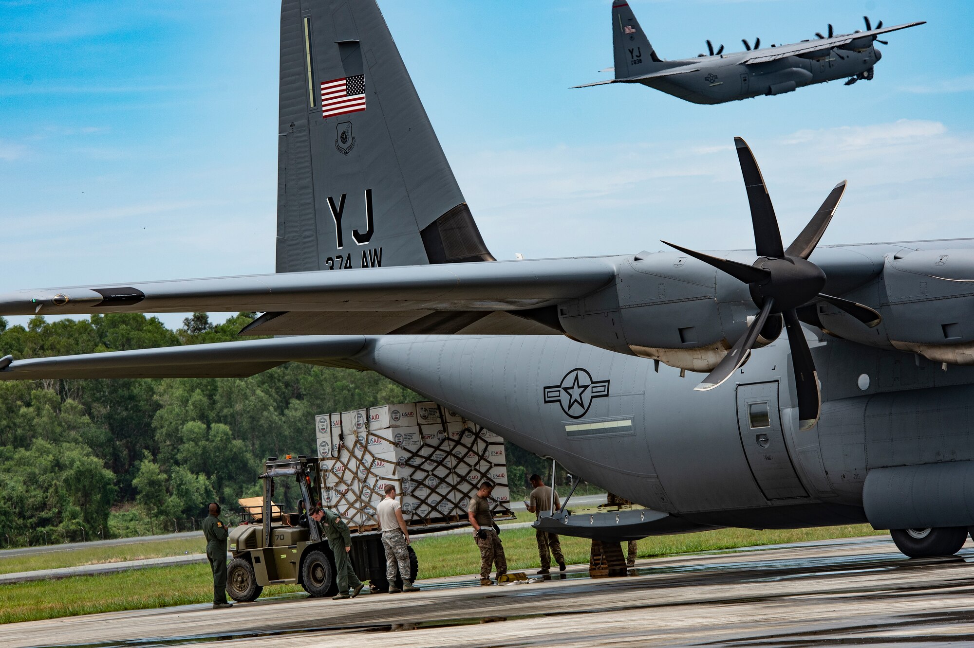 A U.S. Air Force C-130 Hercules from the 374th Airlift Wing at Yokota Air Base, Japan flies over while 36th Mobility Response Squadron aerial porters, from Andersen Air Force Base, Guam load humanitarian supplies in Balikpapan, Indonesia Oct. 14, 2018. (U.S. Air Force photo by Master Sgt. JT May III)