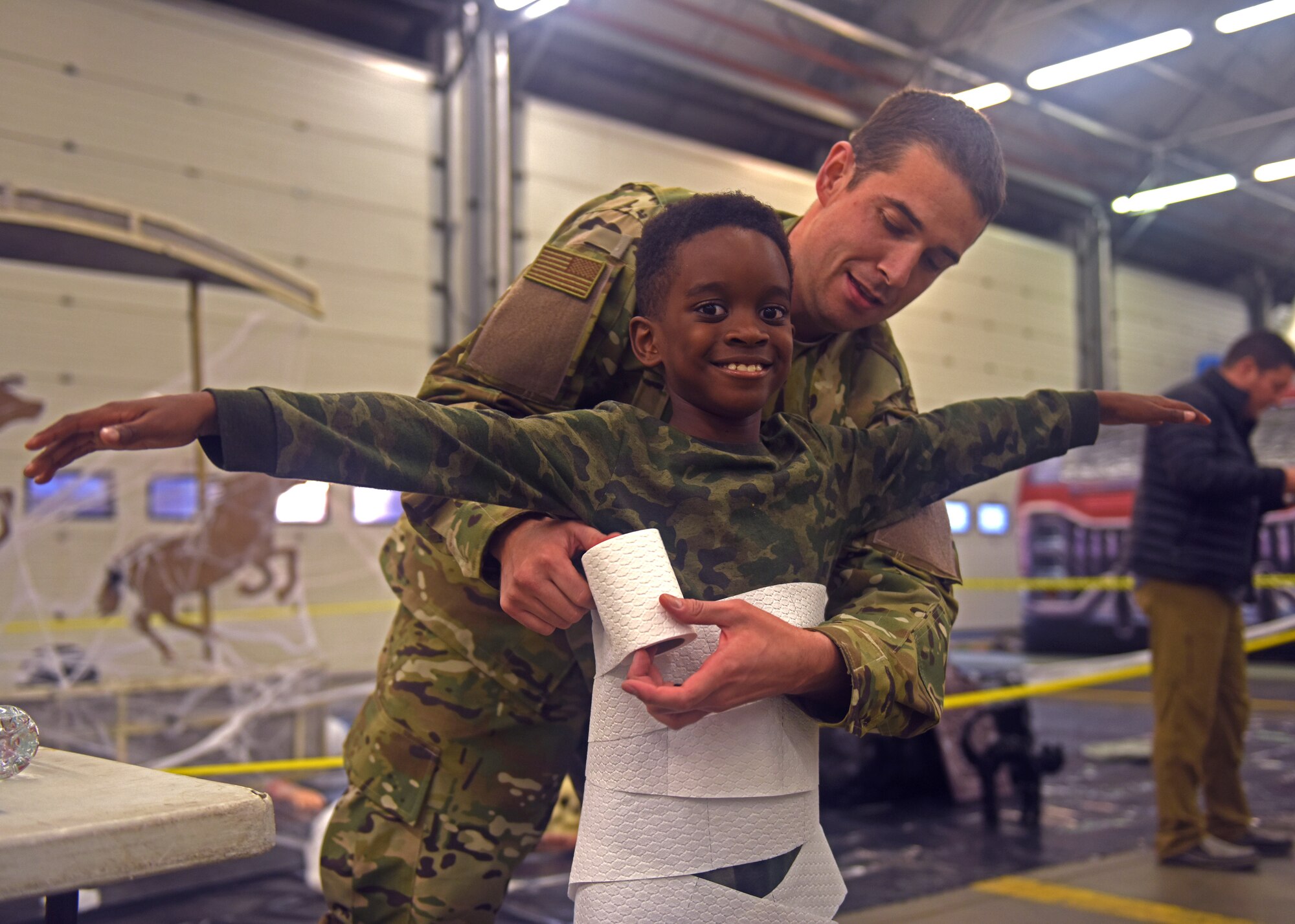 A Team Mildenhall child is wrapped up as a mummy by U.S. Air Force Senior Airman Patrick O’Donnell of the 100th Civil Engineering Squadron during a Halloween-themed Hearts Apart event Oct. 18, 2018, on RAF Mildenhall, England. The event focused on relieving the pressures families sustain when a member is deployed and served as venue to ensure families are connected with the wing’s many helping agencies and resources. (U.S. Air Force photo by Airman 1st Class Brandon Esau)